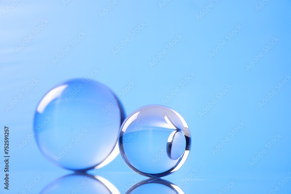 Transparent glass balls on mirror surface against blue background. Space for text Transparent glass balls on mirror surface against blue background. Space for text