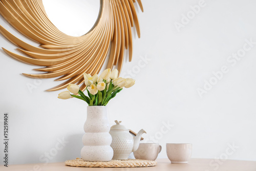 Vase with tulips, teapot and cups on dining table in room