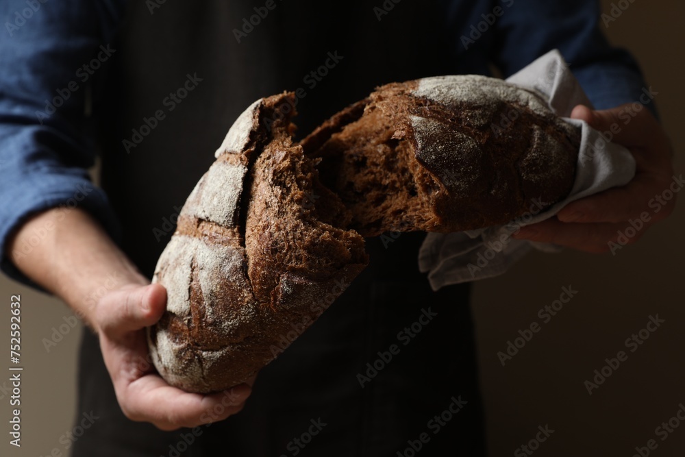 Man breaking loaf of fresh bread on dark background, closeup