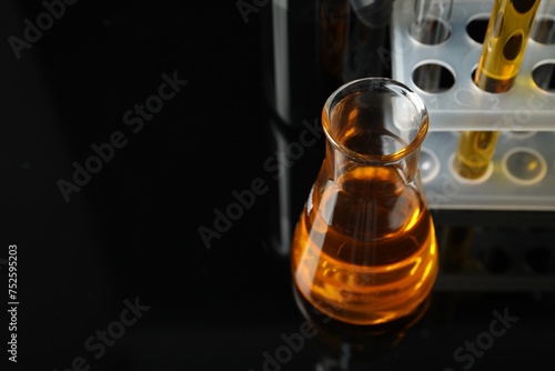 Laboratory glassware with different types of oil on black background, closeup. Space for text photo