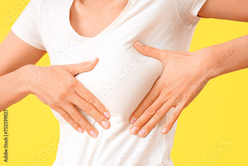 Young woman checking her breast on yellow background, closeup. Cancer awareness concept