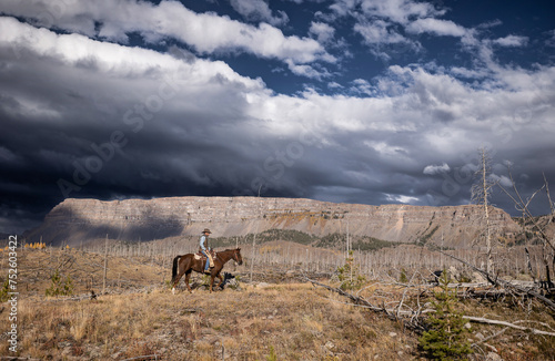 Cowboy riding horse in mountain wilderness outfitter photo