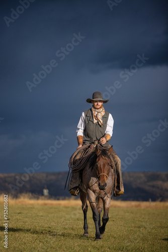 Cowboy riding a roan cow ranch horse with dark storm clouds