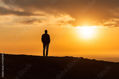 Silhouette of a Lone Person Standing on a Cliff Overlooking a Sunset Sky. Contemplation and Adventure Concept