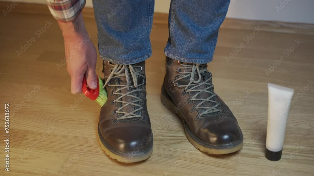 Unrecognizable man cleans brown leather boots with brush and lubricates