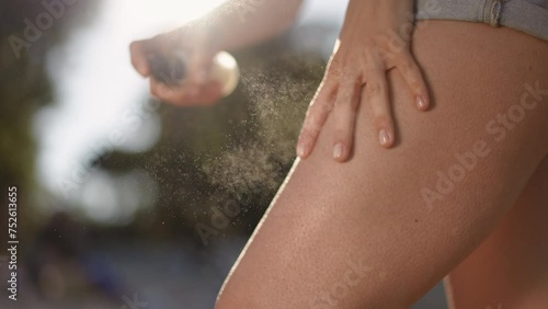 Slow motion. Close-up. An unrecognizable girl in denim shorts sprays sunscreen spray on her thigh from a spray bottle and rubs it with her hand, while standing outdoors
