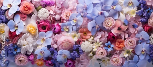 A variety of colorful flowers, including white, violet, pink, and blue, are arranged on a wall against an orchid background. The flowers create a vibrant and eye-catching display.