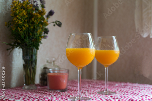 Two vine glasses of orange juise with candle and spring bouquet on the table. Cozy and easy lifestyle. photo