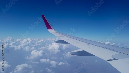 Jaipur, Rajasthan, India-October 25 2023; A Window view of an Aero plane wing gliding above the white clouds through the vibrant blue Sky in India.
