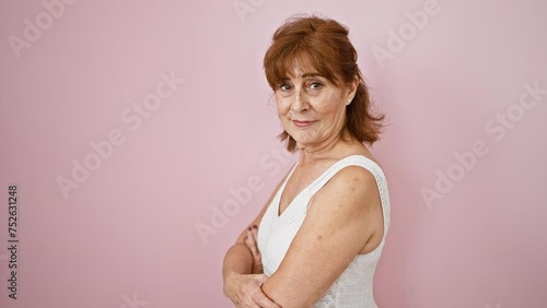 Confident middle-aged woman smirking in an elegant dress, standing offside with a natural, unforced smile. casually posed against an isolated popping pink wall. photo