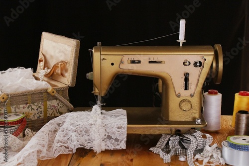 Máquina de coser antigua enhebrada y costurero con encajes, perlas, cintas y adornos photo