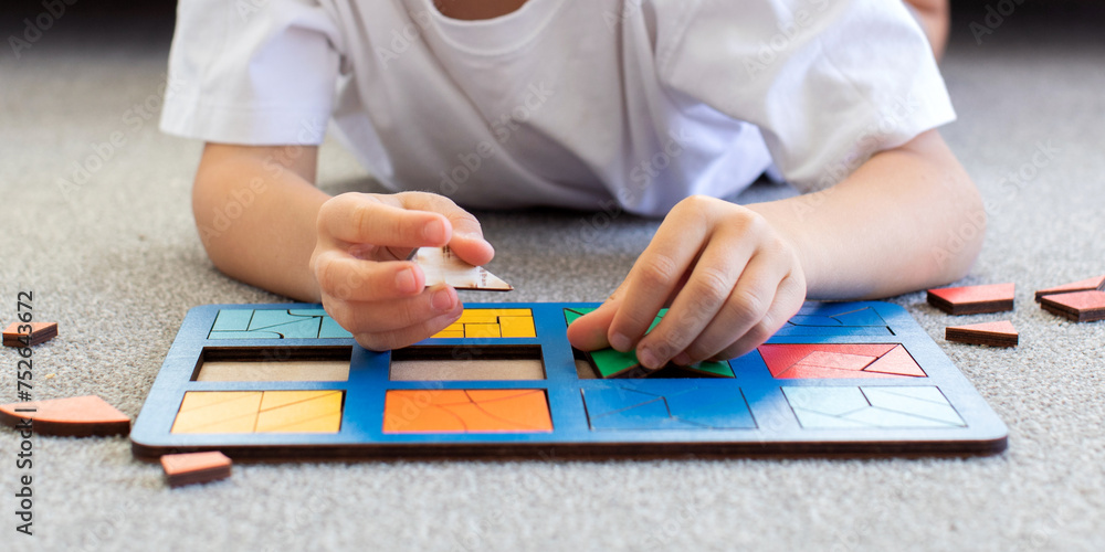 A boy is playing a logical wooden game on the carpet. Montessori educational toys, geometric puzzle A boy is playing a logical wooden game on the carpet. Montessori educational toys, geometric puzzle