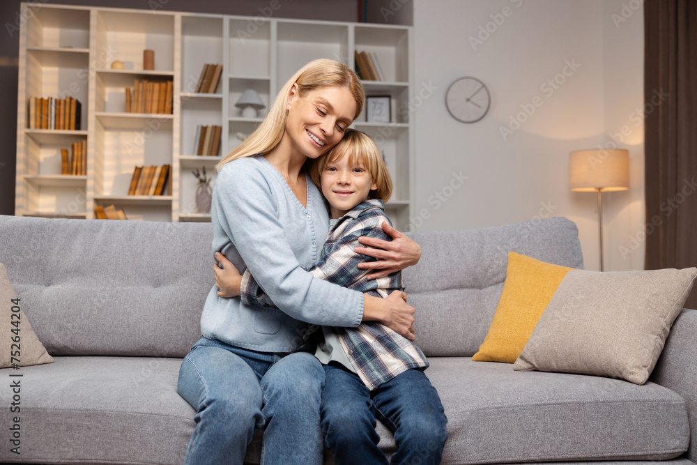 Mother hugging her young son tightly. They are sitting on couch in living room Mother hugging her young son tightly. They are sitting on couch in living room