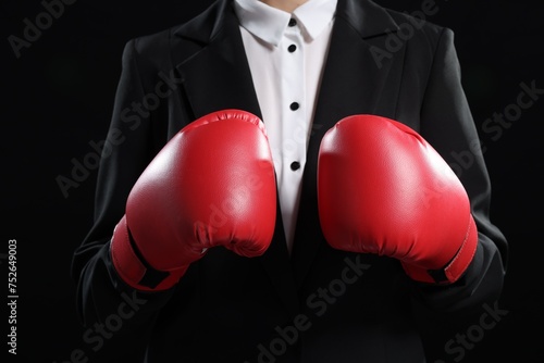 Businesswoman in suit wearing boxing gloves on black background, closeup © New Africa