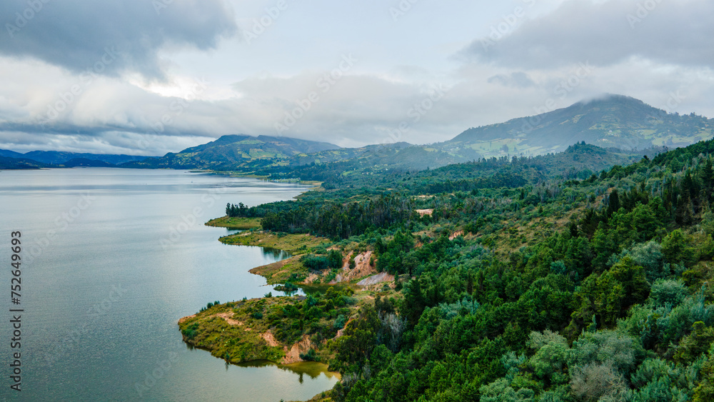 Aerial view of serene Embalse de Tominé, Guatavita, Cundinamarca, surrounded by lush greenery and mountains under a cloudy sky