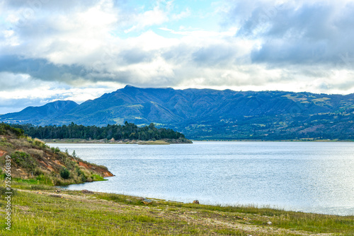 Scenic view of the Tome reservoir in Guatavita, Cundinamarca, showcasing lush mountains, serene waters and a cloudy sky