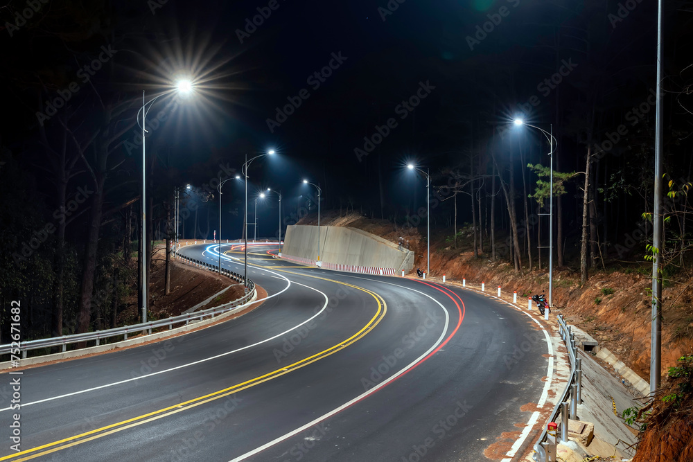 Night scene at the newly widened curved pass in Da Lat, Vietnam illuminated by the headlights of passing cars on a dark night to help traffic flow more smoothly when tourists come here