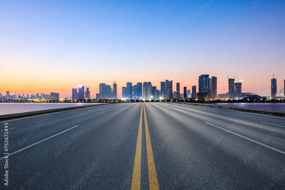 Straight asphalt highway road and city skyline with modern buildings at sunrise