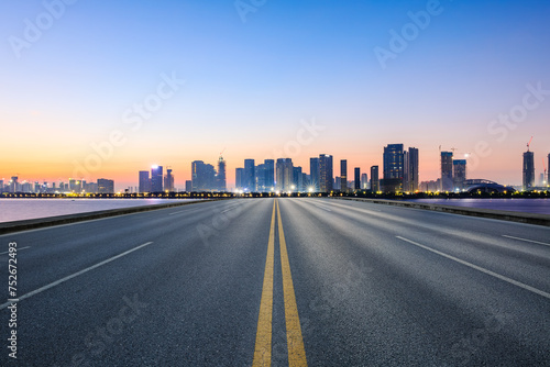 Straight asphalt highway road and city skyline with modern buildings at sunrise