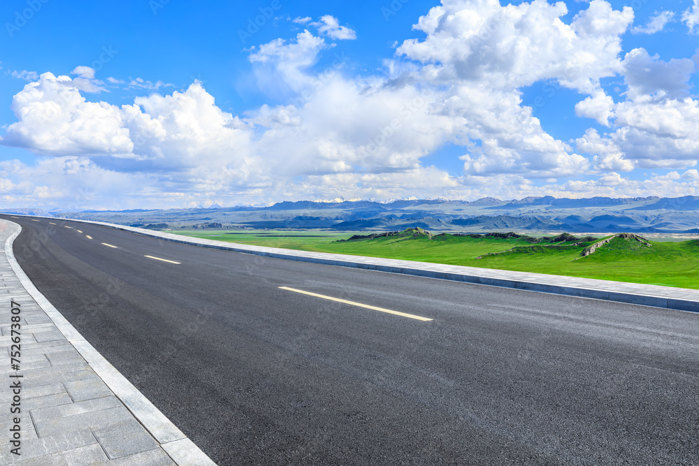 Asphalt highway road and green meadow with mountain nature landscape under blue sky
