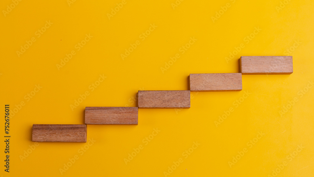 Flat lay of wooden blocks in the shape of a staircase step on a yellow background with copy space. Growth or development step by step for success in business financial or education concept. Flat lay of wooden blocks in the shape of a staircase step on a yellow background with copy space. Growth or development step by step for success in business financial or education concept.