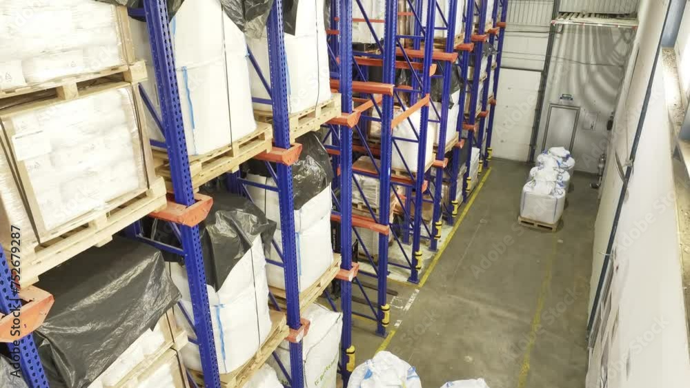 Inside a warehouse: many shelves laden with neatly stacked pallets, anonymous containers. Camera looking up while descending. Logistics, industrial technology, goods management and storage. Inside a warehouse: many shelves laden with neatly stacked pallets, anonymous containers. Camera looking up while descending. Logistics, industrial technology, goods management and storage.