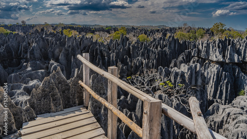 The unique Nature Reserve Tsingy De Bemaraha. Incredible grey karst rocks stretch to the horizon. In the foreground is a wooden observation deck with a railing. Clouds in the blue sky. Madagascar. photo