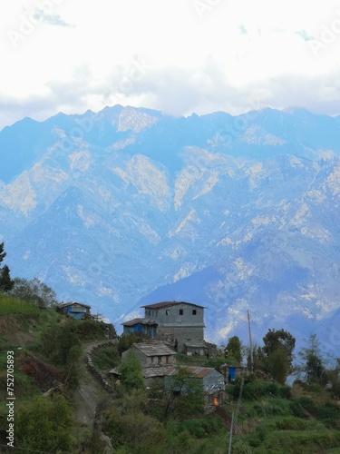 A charming house perched on a scenic hill, framed by majestic mountains in the backdrop, offering serene beauty.