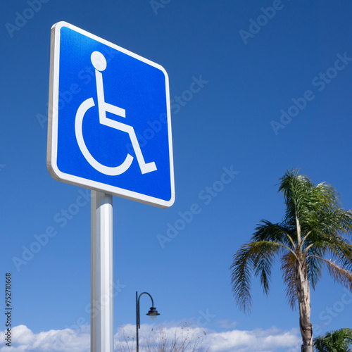 Blue Handicapped Parking Sign with Blue Sky, Palm Tree, Light Post and Clouds Background