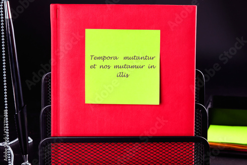 Tempora mutantur et nos mutamur in illis Translated from Latin, it means Times are changing, and we are changing with them. on a yellow sticker on a red notebook. Concept photo photo