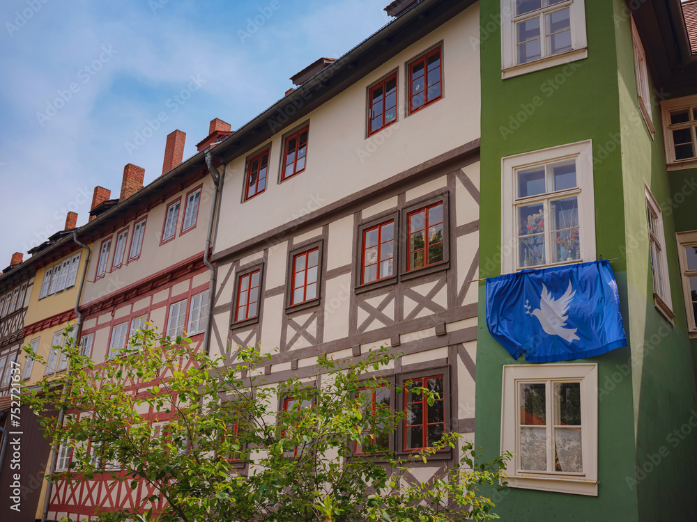 Fototapeta premium spring trip to Europe. scenic view to facade of old historic houses somewhere in Erfurt city, blue flag with a dove of peace that residents of house hung on their facade