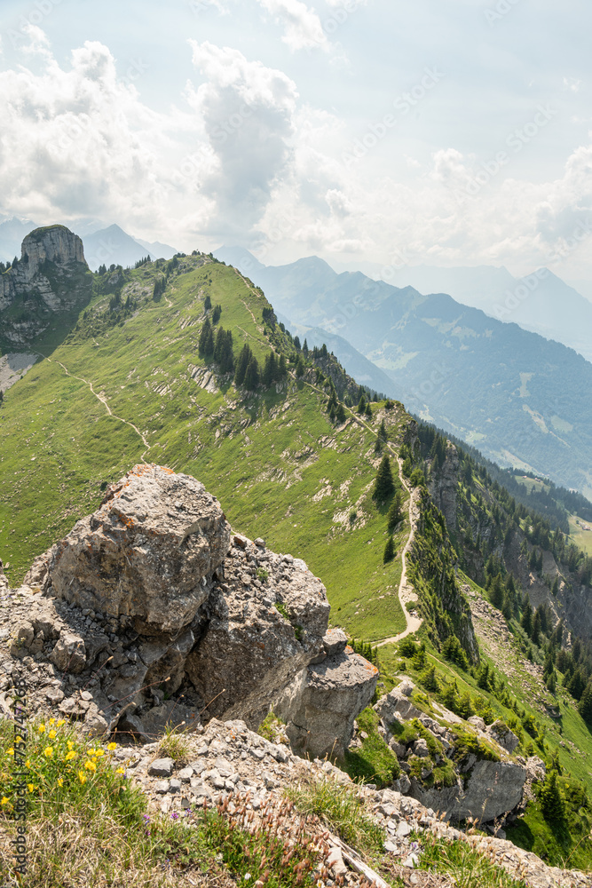 Fototapeta premium Summer view from Oberschildhorn mountain towards Schynige Platte in the Jungfrau region. Alpine mountains with hiking trail. Rocks in the foreground. Swiss Alps landscape.