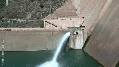 Dam and water reservoir. Howell bunger valve in operation. Dam discharging water. Panoramic aerial view of the dam and hydroelectric plant rising. Dolly out aerial view. Renewable energies. photo