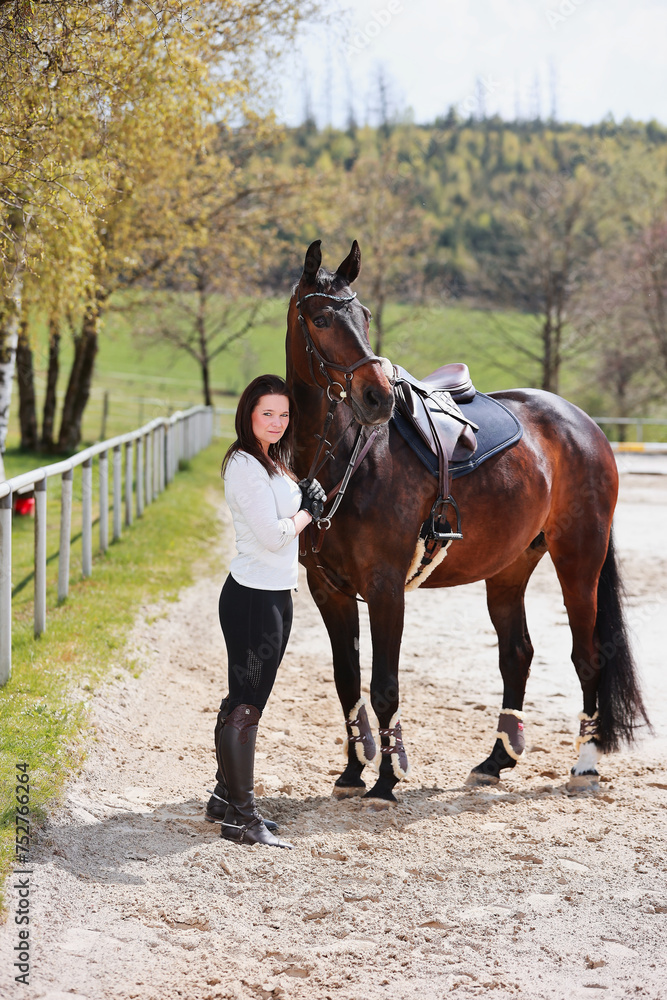 Young Frtau rider with brown long hair in portrait with her horse on the riding arena. Young Frtau rider with brown long hair in portrait with her horse on the riding arena.