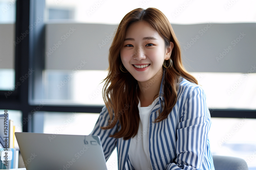 a beautiful korean women smiles while using her laptop in the office a beautiful korean women smiles while using her laptop in the office