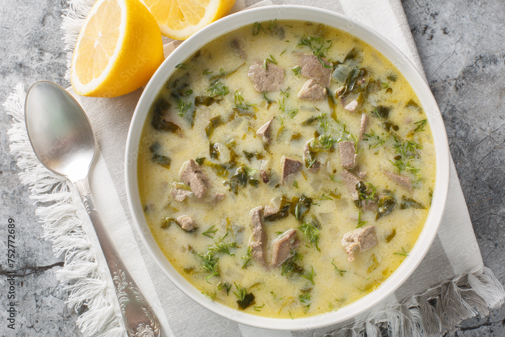 Greek Easter soup with lamb offal, herbs, seasoned with egg and lemon sauce close-up in a bowl on a marble table. Horizontal top view from above