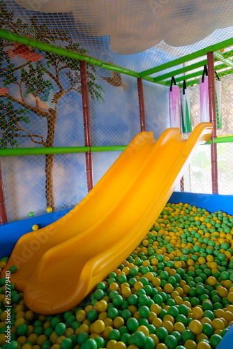 Yellow slide at indoor playground against colourful plastic balls. Yellow sliding board for kids. Empty colorful slides fun activity holiday entertainment.