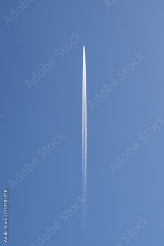 Distant Passenger Jet Plane Flying at High Altitude on a Clear Blue Sky Leaving a White Smoke Trace of Contrail Behind
