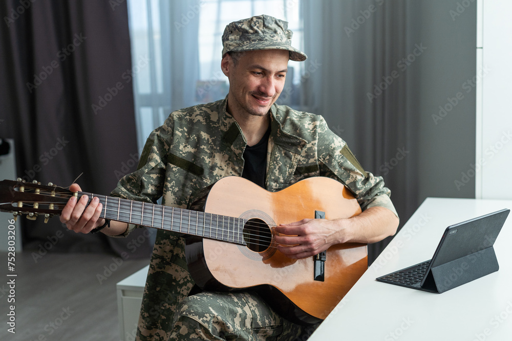 Obraz premium Cheerful smiling young military man wearing khaki uniform holding guitar.