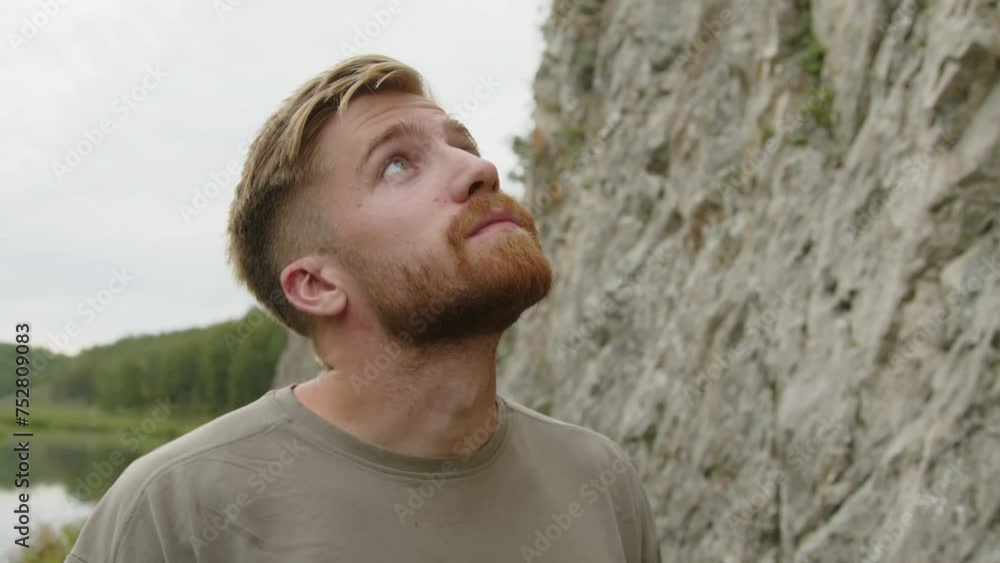 Tilt up shot of young bearded man checking climbing gear, looking up and going to rock Tilt up shot of young bearded man checking climbing gear, looking up and going to rock