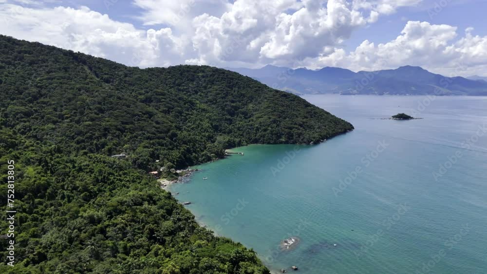 Aerial shot drone orbits to the right around coast of forested island Aerial shot drone orbits to the right around coast of forested island