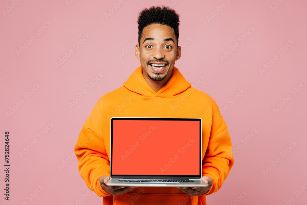 Young surprised IT man of African American ethnicity wear yellow hoody casual clothes work hold use blank screen workspace area laptop pc computer isolated on plain pink background. Lifestyle concept. Young surprised IT man of African American ethnicity wear yellow hoody casual clothes work hold use blank screen workspace area laptop pc computer isolated on plain pink background. Lifestyle concept.