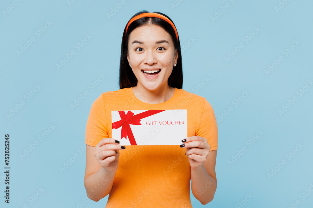 Φωτογραφία Young surprised woman of Asian ethnicity wear orange t-shirt casual clothes hold gift certificate coupon voucher card for store isolated on pastel light blue cyan background studio