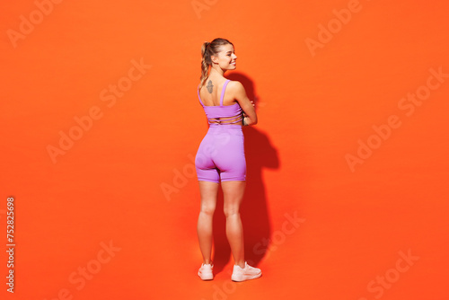 Fototapeta Naklejka Na Ścianę i Meble -  Full body back rear view fun young fitness trainer instructor woman sportsman wear purple top clothes train in home gym look aside isolated on plain orange background. Workout sport fit abs concept.
