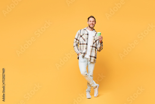 Full body young Caucasian man wear brown shirt casual clothes hold takeaway delivery craft paper brown cup coffee to go isolated on plain yellow orange background studio portrait. Lifestyle concept.