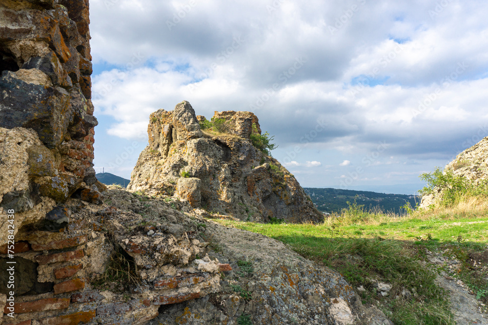 On the top of Kojori fortress. Ruins of the wall and tower made from rock and bricks.  Landscape of nearby mountains and villages. Clear blue sky and clouds. Georgia.