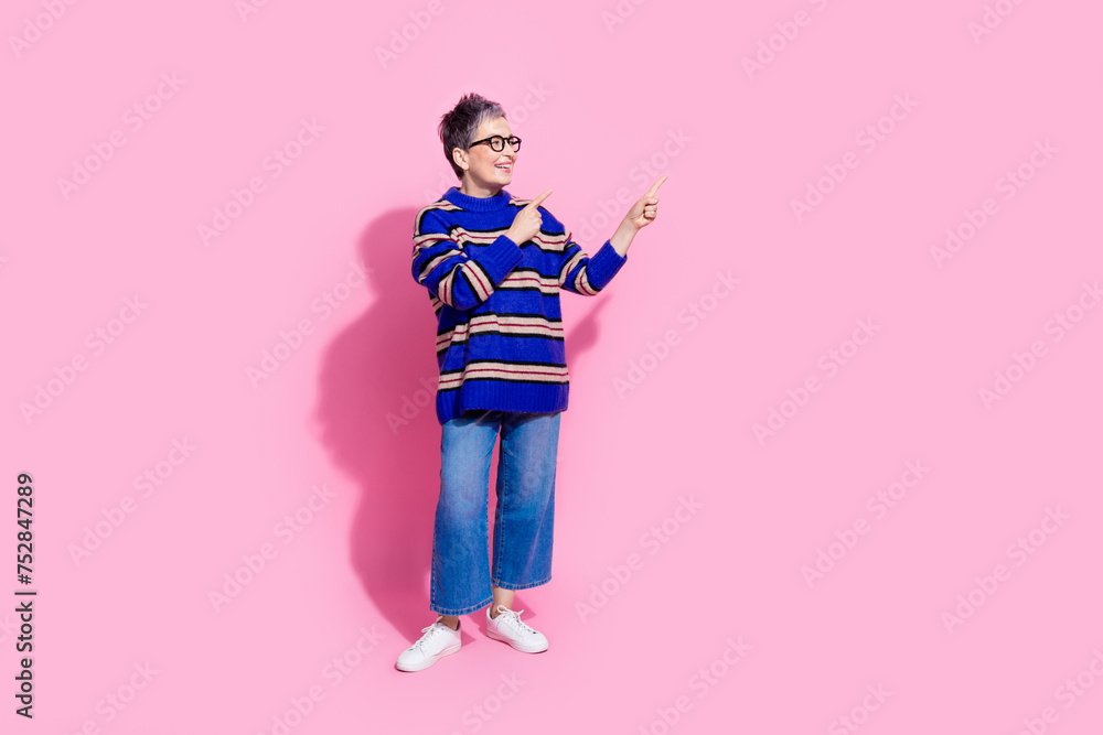 Full body photo of attractive pensioner woman point look empty space dressed stylish blue striped clothes isolated on pink color background Full body photo of attractive pensioner woman point look empty space dressed stylish blue striped clothes isolated on pink color background