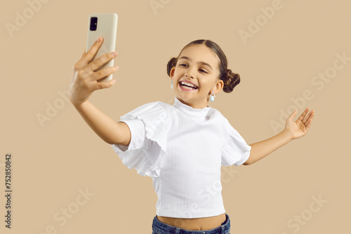 Smiling teen girl child isolated on nude brown studio background talk on video call on cellphone. Happy cute teenage kid speak on webcam modern smartphone. Online communication concept.