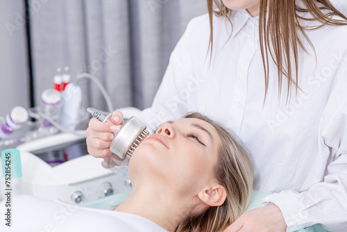 Pretty young blonde woman client lying with closed eyes and getting stimulating beauty facial treatment during rf-lifting procedure at clinic. Radiofrequency face lifting. Hardware antiaging procedure