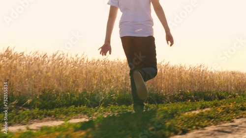 Unrecognizable boy teenager running on dirt road at natural sunlight autumn summer field back view closeup. Happy male teen relaxing outdoor enjoy freedom leisure activity sunny meadow sky landscape